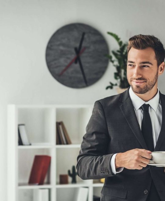 happy-young-businessman-with-cup-of-coffee-at-offi-JB7JNZ8.jpg